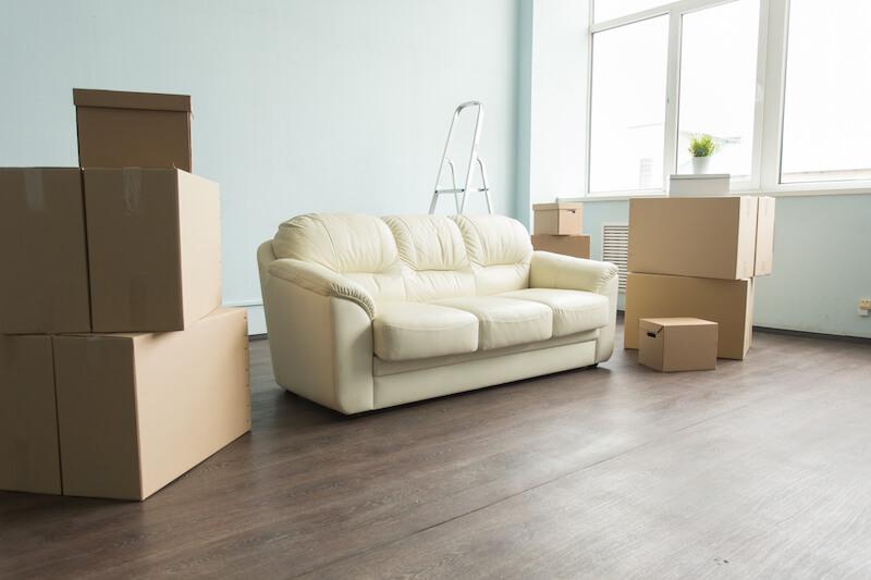 A white sofa surrounded by moving boxes in a bright room.