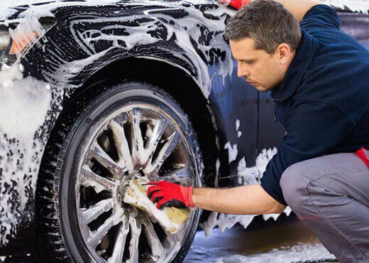 Man cleaning a car's wheel with a red glove.