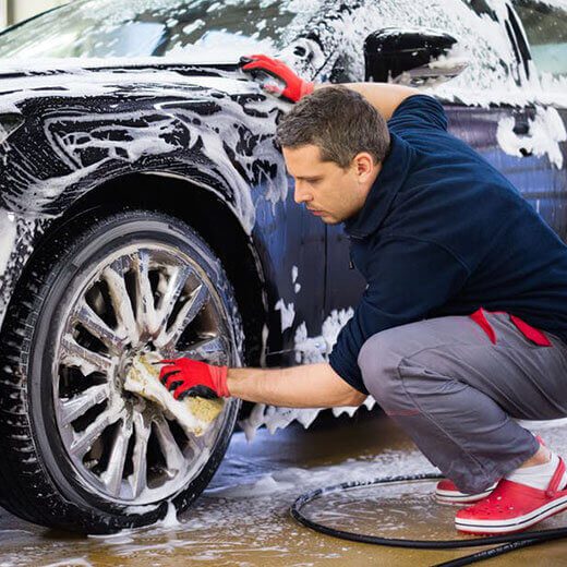 Man washing car wheels with soap and sponge outdoors.