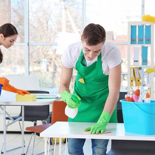 Two people cleaning a classroom with gloves and spray bottles.