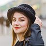 Young woman wearing a black hat and gray jacket outdoors.
